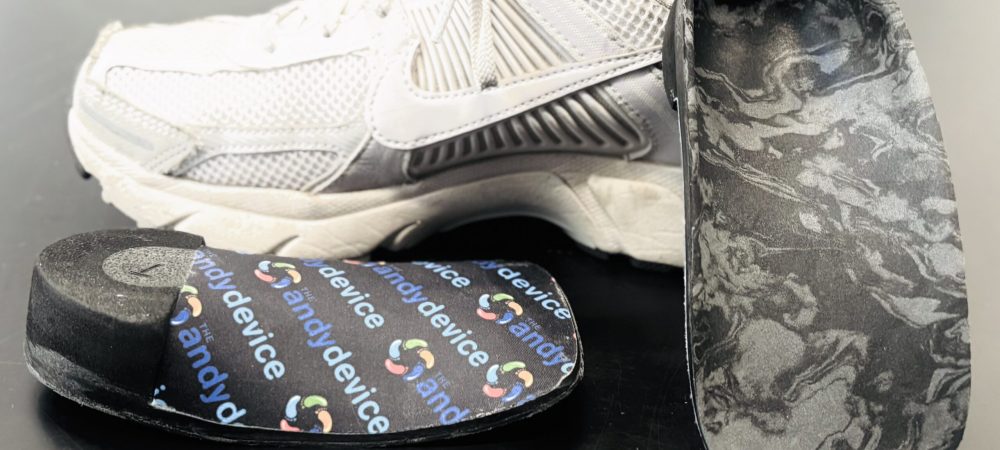 “Custom pediatric orthotics with black marbled support surface and branded top layer displayed alongside a white athletic shoe.”